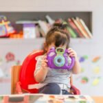 girl holding purple and green camera toy