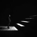 grayscale photo of man standing in front of stairs