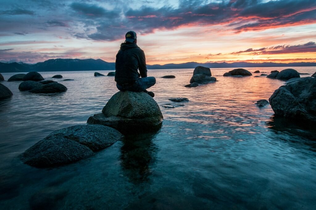 man sitting on rock surrounded by water - What does the Bible say about meditation?